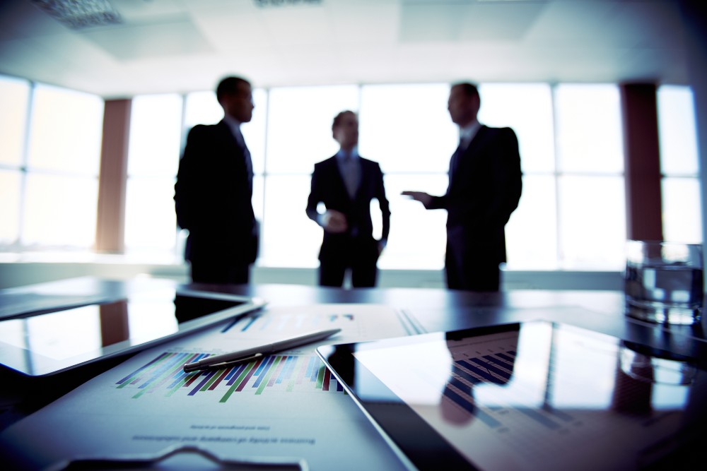 three men talking in a conference room with data and tablets on the table in front of them