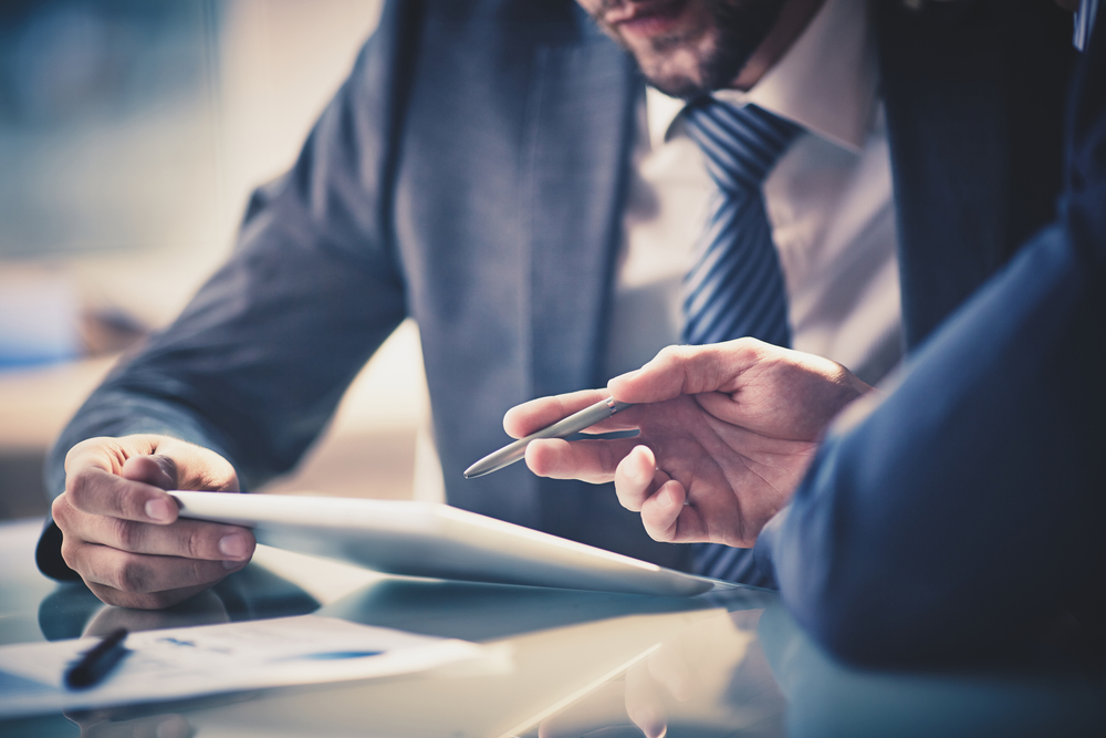 Image of two young businessmen using touchpad at meeting